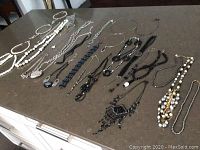 Photo showing a wide variety of costume jewelry necklaces in different colors including white, black, silver, and mixed beads, arranged on a dark surface.