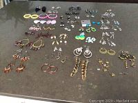 Full assortment of approximately 60 pairs of costume earrings laid out on flat surface.