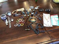Full lot overview showing rings, watches, hair clips, sunglasses, foot jewelry, glass beads, and necklaces spread out on table.