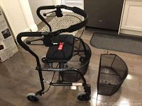 Full view of the black Nexus walker showing padded seat, handles with brakes, four wheels, and two wire baskets.