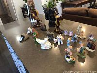 Overview of various animal figurines on a table including ceramic horses, resin horses, dogs, elephants, angel figures, and glass swan.
