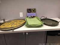 Lot contents on counter showing two metal serving trays, green fabric placemats stacked in center, and a book standing upright