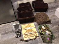 Five dark brown wicker baskets and assorted home decor including fabric remnants, door handle and decor accents laid on floor.