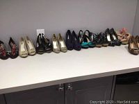 Photo showing ten pairs of women's heeled sandals and closed toe shoes arranged in a row on a white counter.