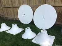 Two round white fiberglass tabletop pieces with central umbrella holes and four base sections arranged on grass.
