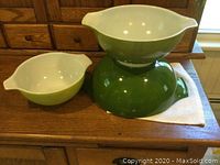 Three stacked Pyrex Verde Green Cinderella mixing bowls with white interiors shown on a wooden surface