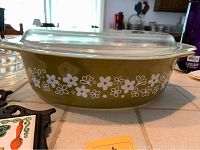 Side view of the vintage Pyrex Crazy Daisy oblong covered casserole dish showing the olive green color and white floral pattern with clear lid.