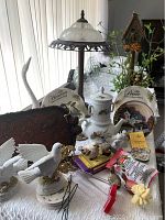 Photo showing full lot including white ceramic bird figurines, angel decor plates, stacked white teapot set, rustic birdhouse with plants, vintage lamp, and assorted decorative pieces.