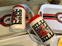 Four rectangular white trays with handles and Buffalo Bills logo, with two large white mugs featuring red accents and Buffalo Bills helmet and text logos.