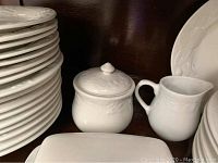 Stack of white plates, creamer and sugar bowl, showing embossed leaf and floral pattern detail