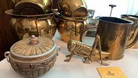 View of four brass pots stacked and grouped, with a decorative wooden trinket box with lid and a brass cricket figurine in front.