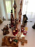 Wide view showing multiple wooden churches, snowman figurine, wooden deer, ceramic angels, red glass candle holders, and small wooden houses on white surface.