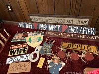 Overview of collection of various wooden signs with themes of apples, home, wife, and marriage phrases, laid out on a red cloth.