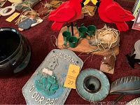 Photo showing a wooden candle holder with two red cardinal birds and four green candle cups, gray frog plaque, and ceramic bowl and dish on red carpet.
