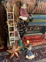 Wide view of fireplace hearth with two wooden signs leaning, metal star, fabric dolls, small ladder and dried flowers decor