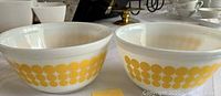Front view of two vintage Pyrex mixing bowls with yellow dot pattern on white glass surface