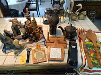 Wooden and resin moose figurines, candle holders, napkin holders and rings, wooden kitchen utensils, metal tea pot, and other wooden decorative items arranged on a tiled surface.