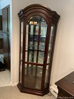 Front view of Philip Reinisch serpentine curio cabinet showing curved wooden frame, glass door and panels, glass shelves and mirrored back.