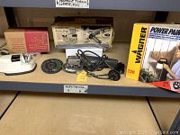 Photo showing Cory electric knife sharpener, Craftsman 4.5 inch angle grinder with grinding wheels, and boxed Wagner paint sprayer on shelf.