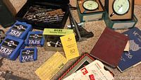 Overview of tools and handbook laid out on floor showing two dial gauges, blue tap cases, yellow reloading equipment box, various small items and a red Machinery's Handbook.