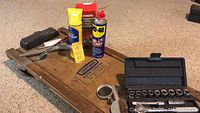 Full view of the craftsman auto creeper wooden board with metal handle, socket set case, and automotive care products arranged on the floor.