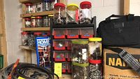 Multiple plastic jars on shelves containing various fasteners such as screws, nails, nuts, and bolts along with a black tool bag.