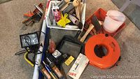 Full lot including orange cord wheel, work light, caulking gun, paint trays, brushes, rollers, and hand tools arranged on floor.