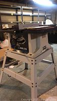 Full view of Delta Shop Master table saw on white metal stand showing brand name.