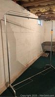Full view of metal clothing rack against basement wall showing vertical poles and horizontal hanging bar.