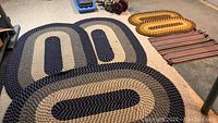 Photo showing three oval braided rugs in navy and beige colors, neatly stacked.