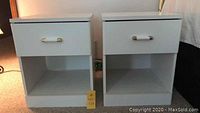 Front view of the two white veneer bedside tables showing one drawer and open shelf per table.