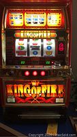 Front view of King Of Fire slot machine with illuminated display, spinning reels showing symbols including cherries, crowns, sevens, and letters.