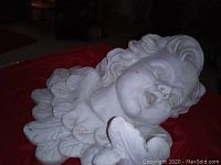 Close-up front angle of off white stone cherub angel face sculpture lying sideways showing detailed hair and hand.