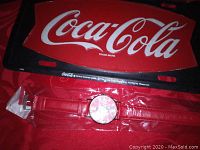 Photo of red Coca-Cola branded license plate and new Coca-Cola watch with red strap still sealed in plastic