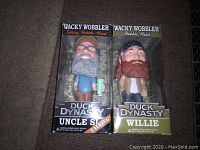 Photo of Duck Dynasty Uncle Si talking bobble head and Willie non-talking bobble head in boxes on carpet
