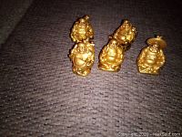 Front view of five gold miniature Buddha statues arranged on carpet.