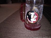 Front side of the clear glass mug with Florida State Seminoles head logo, showing red handle and base with ice mud inside.