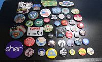 Top view of 46 assorted button pins and magnets on black surface showing a variety of pop culture, patriotic, and location themes.