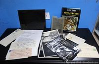 Overview of lot on black table: book, black negative holder, plastic sleeve with document, photos, letters and envelopes