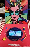 Interior of pop-up Rocketman box showing graphic portrait and built-in screen playing video