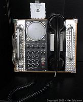Front view showing phone layout with speaker, big buttons, controls, and handset on metal and wood frame.