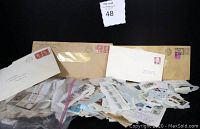 Wide view of the plastic bag filled with assorted postage stamps and ephemera with four vintage postal envelopes behind it showing different stamps and postal markings.