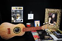 Photo shows natural wood Kangaroo soprano ukulele with four strings, Slash Pop vinyl figure in box, small drum decoration, gold framed color photo of Gloria Estefan, and portion of music magazines.