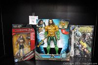 Front view of the three items displayed, showing Aquaman action figure in large packaging, Justice League Aquaman figure sealed, and comic book inside a protective bag.