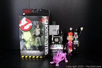 Photo showing five Ghostbusters items: Ray Stantz action figure in box, Proton Pack on stand, Police Officer and Ghost figures, Old Lady and Ghost figures, and Purple Ghost Slime figure.