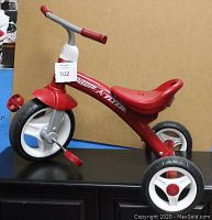 Side view of red Radio Flyer child's tricycle, highlighting plastic wheels, pedals, and seat.