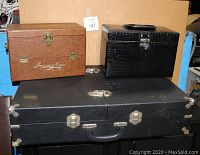 Three storage boxes stacked, showing black collectibles case on bottom, brown Garcia Vega cigar box and brown makeup or arts and crafts box on top