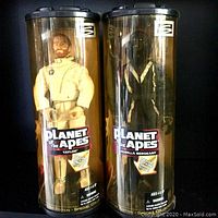 Front view of two sealed Planet of the Apes Special Collector Edition figures labeled Taylor and Gorilla Sergeant, in clear cylindrical packaging with black lids and rotating stands, showing brand logos and warnings.