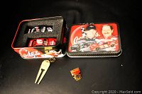 Open Coca Cola metal collector tin showing Dale Earnhardt and Dale Earnhardt Jr with their racing cars and foam inserts holding two diecast racing cars in original boxes, plus an Olympics pin and can opener outside the tin.