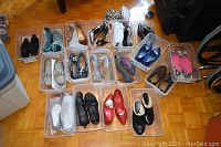 Wide shot of 21 pairs of women's shoes arranged in transparent plastic containers on floor.